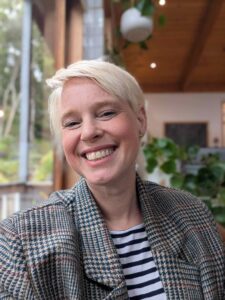 Johanna Skelton. A smiling blond woman in a brown blazer and stripy top