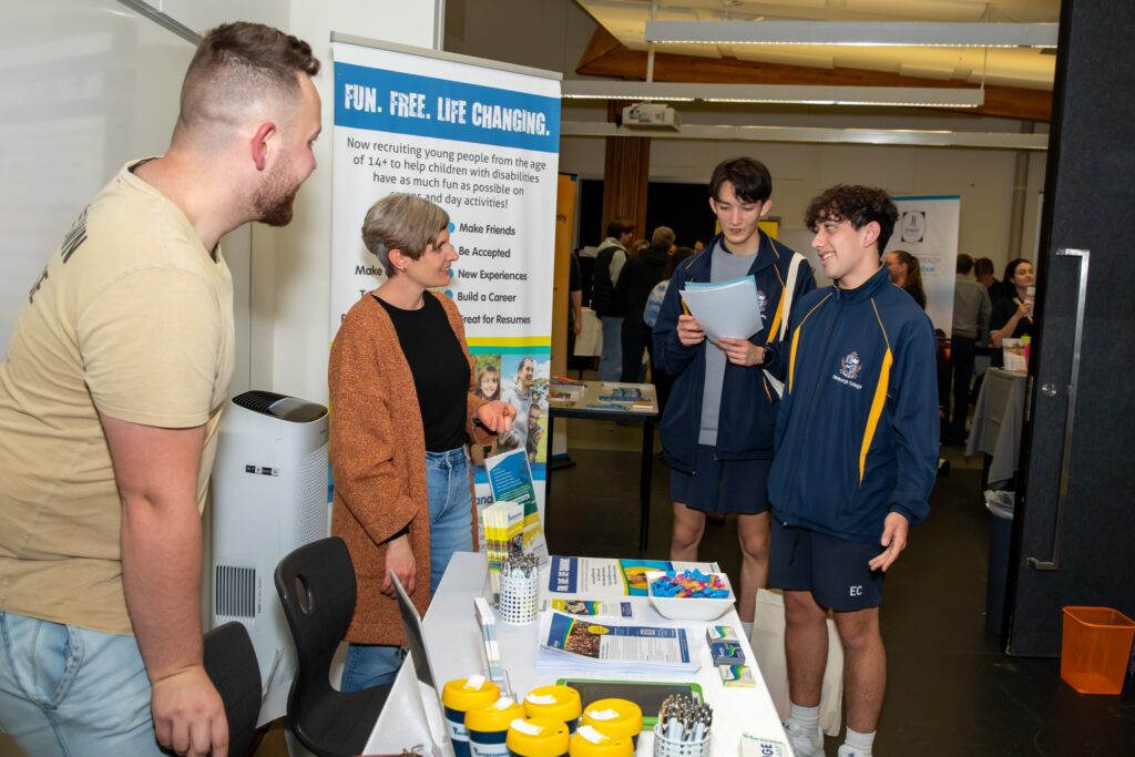 Photo of people at career expo. Two students talking to two people behind a stall at the expo.
