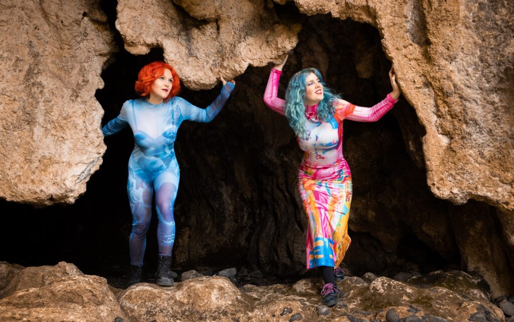 Photo of Charlie Needs Braces dressed in colourful full body against the skin suit/dress emerging out of a cave.